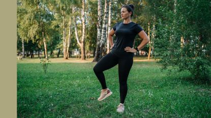 Woman doing hip airplane exercise in activewear standing in green park in the sunshine