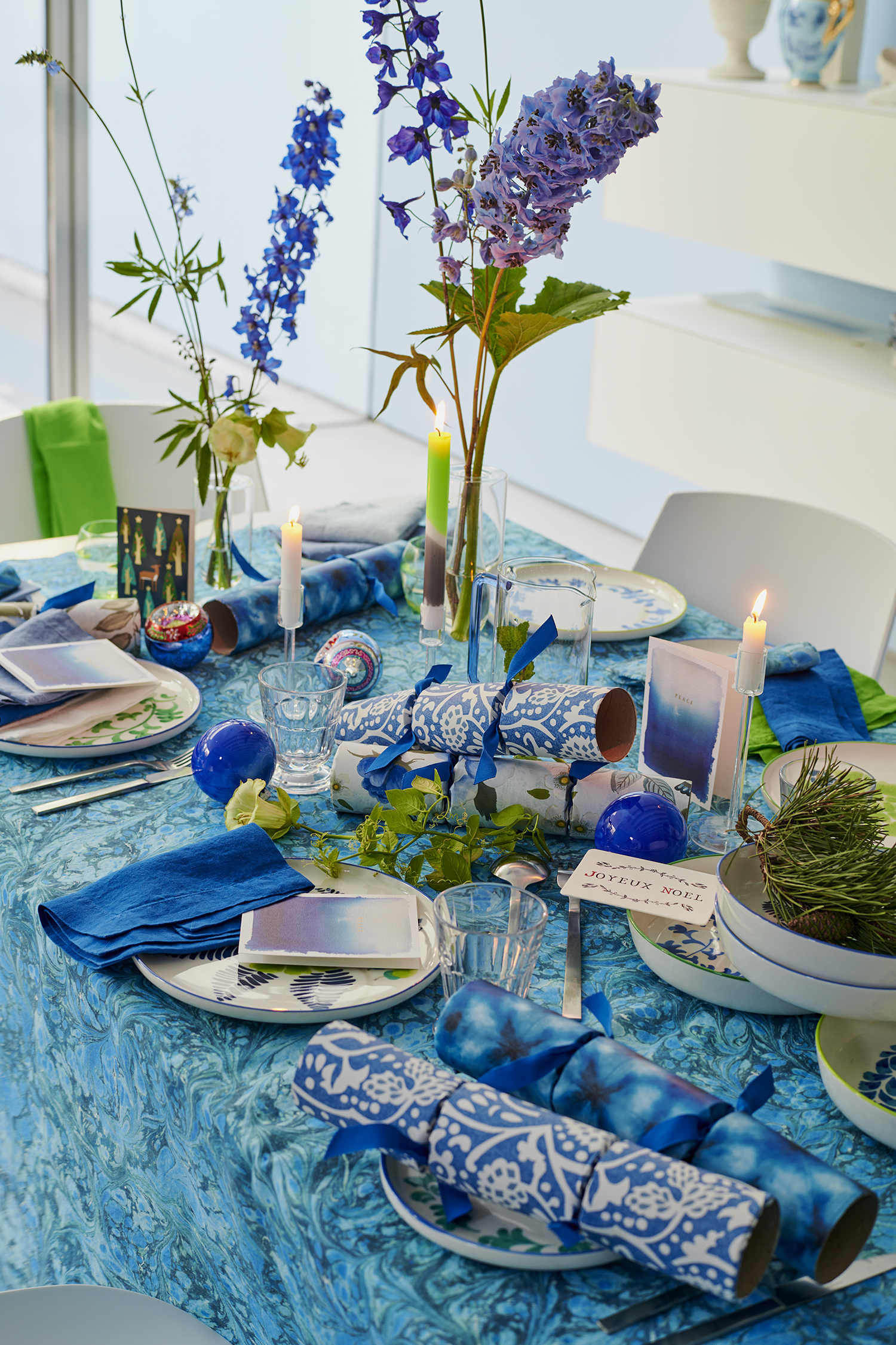 bright blue christmas table setting with patterned crackers, blue patterned tablecloth, blue flowers, moss, and candlesticks