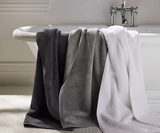 Three Turkish towels - one black, one gray, one white - draped over a bathtub.