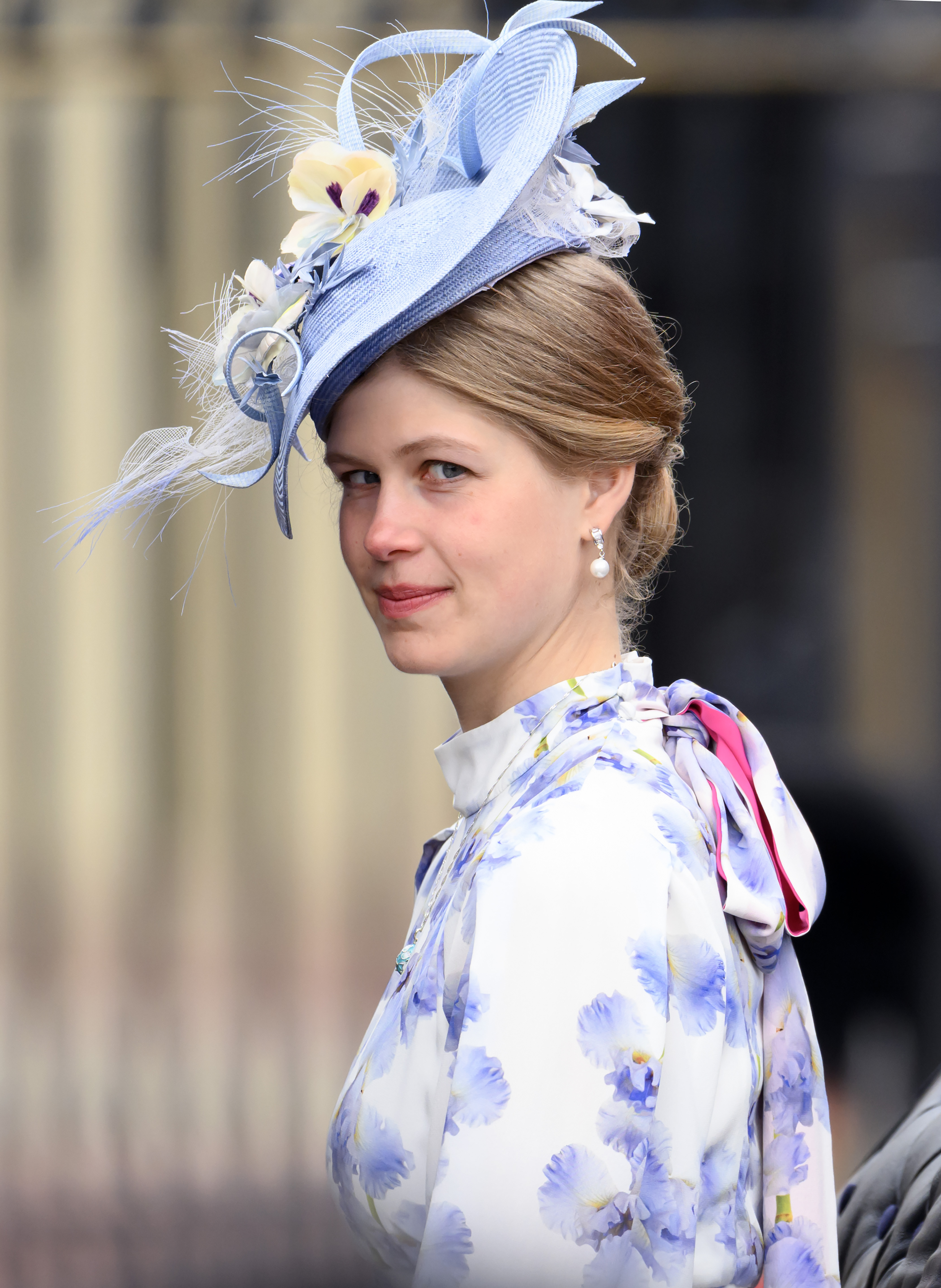 Lady Louise wearing a blue hat and white dress, looking into the camera
