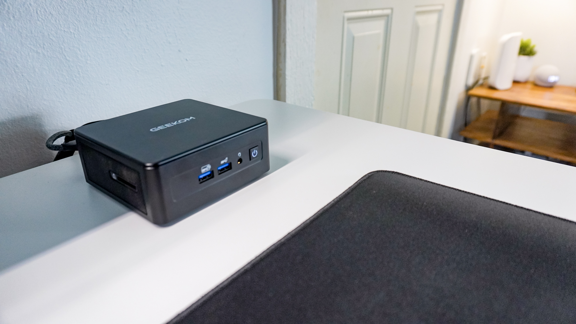 The Geekom IT15 mini PC on a desk with the eero Max 7 mesh Wi-Fi 7 router in the background