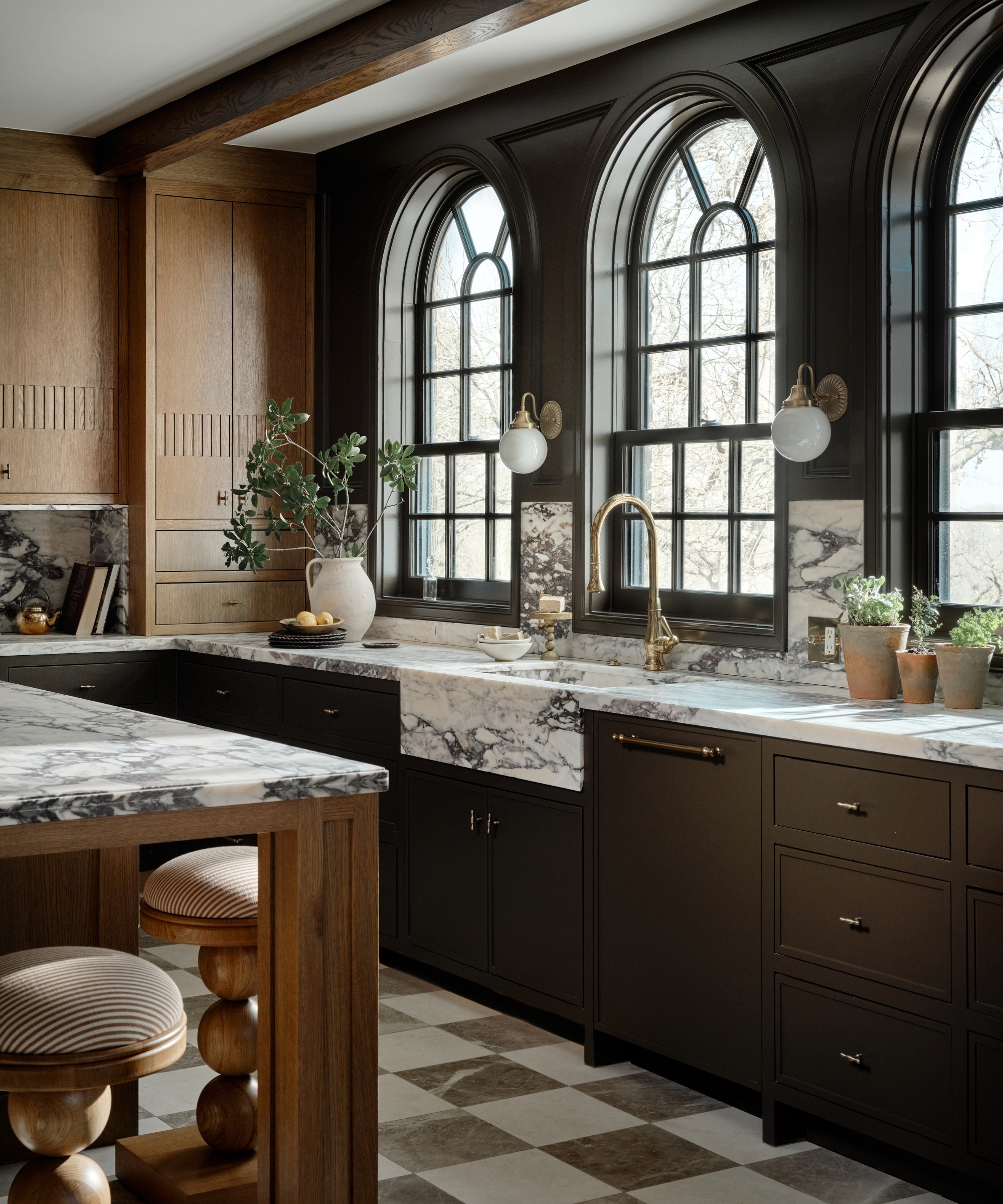 A traditional kitchen with wooden cabinets, arched windows, round lighting, and checkerboard floors