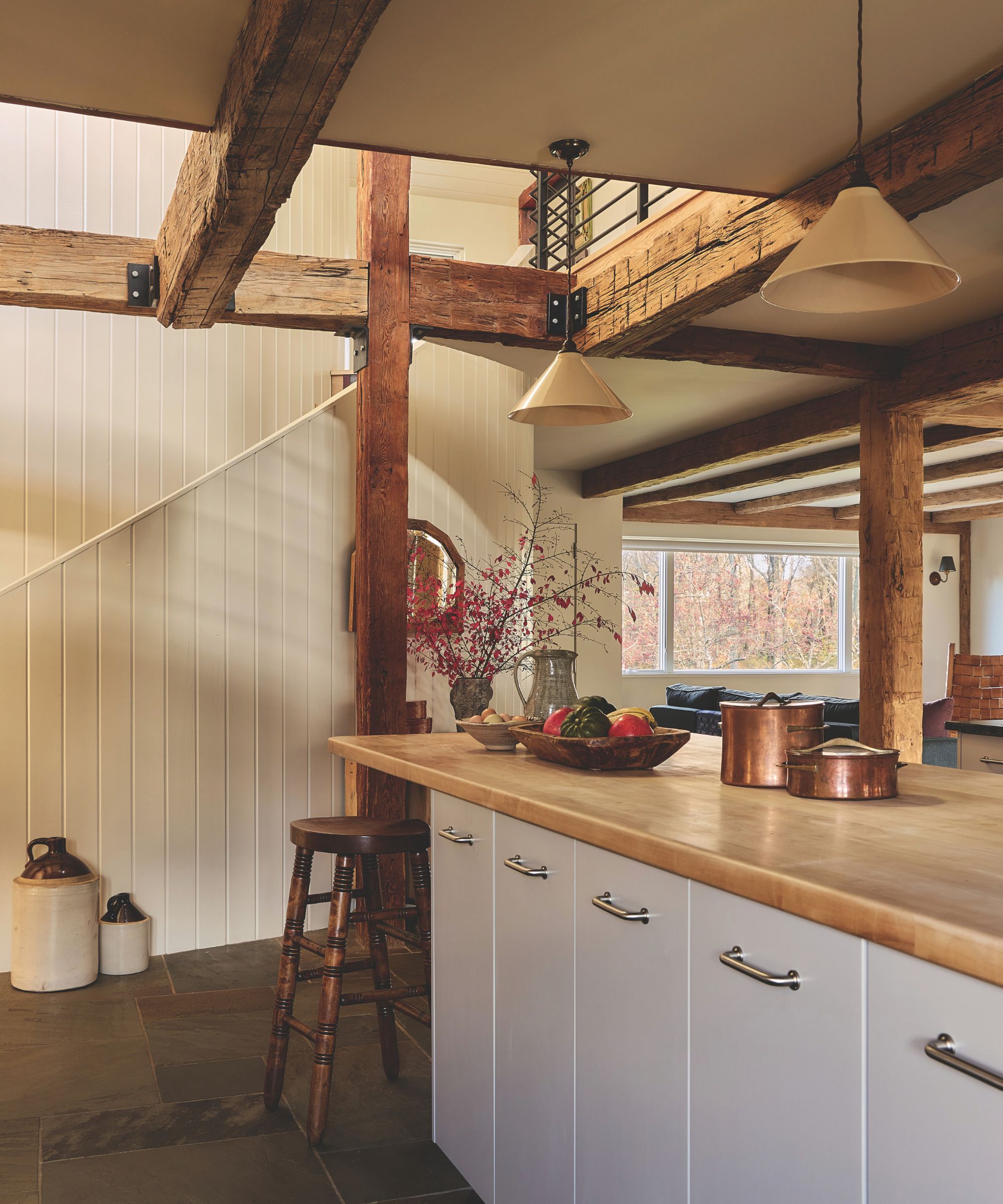 Kitchen island with smooth light wood countertop, pendant light, wooden barstool, and copper pots set against exposed timber beams.