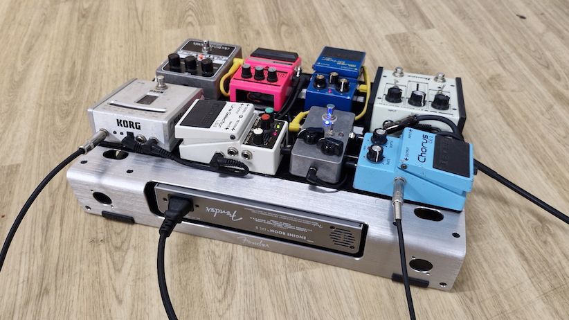 A Fender Professional Small pedalboard with pedals on a wooden floor