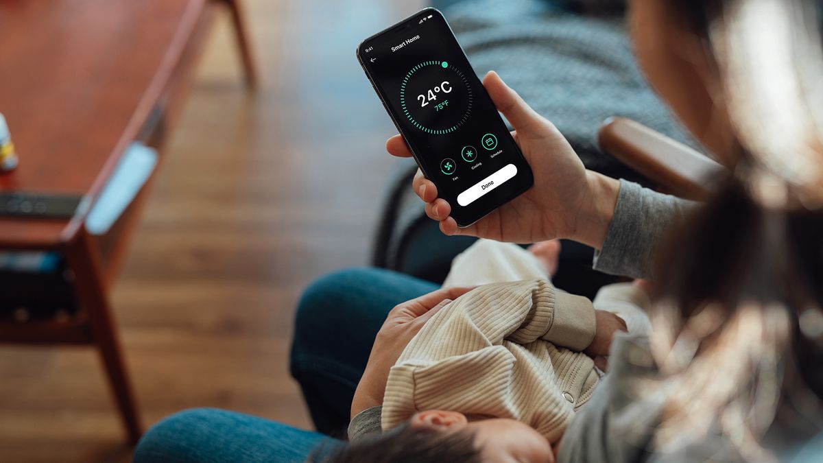 Woman holding smartphone and looking at temperature of home