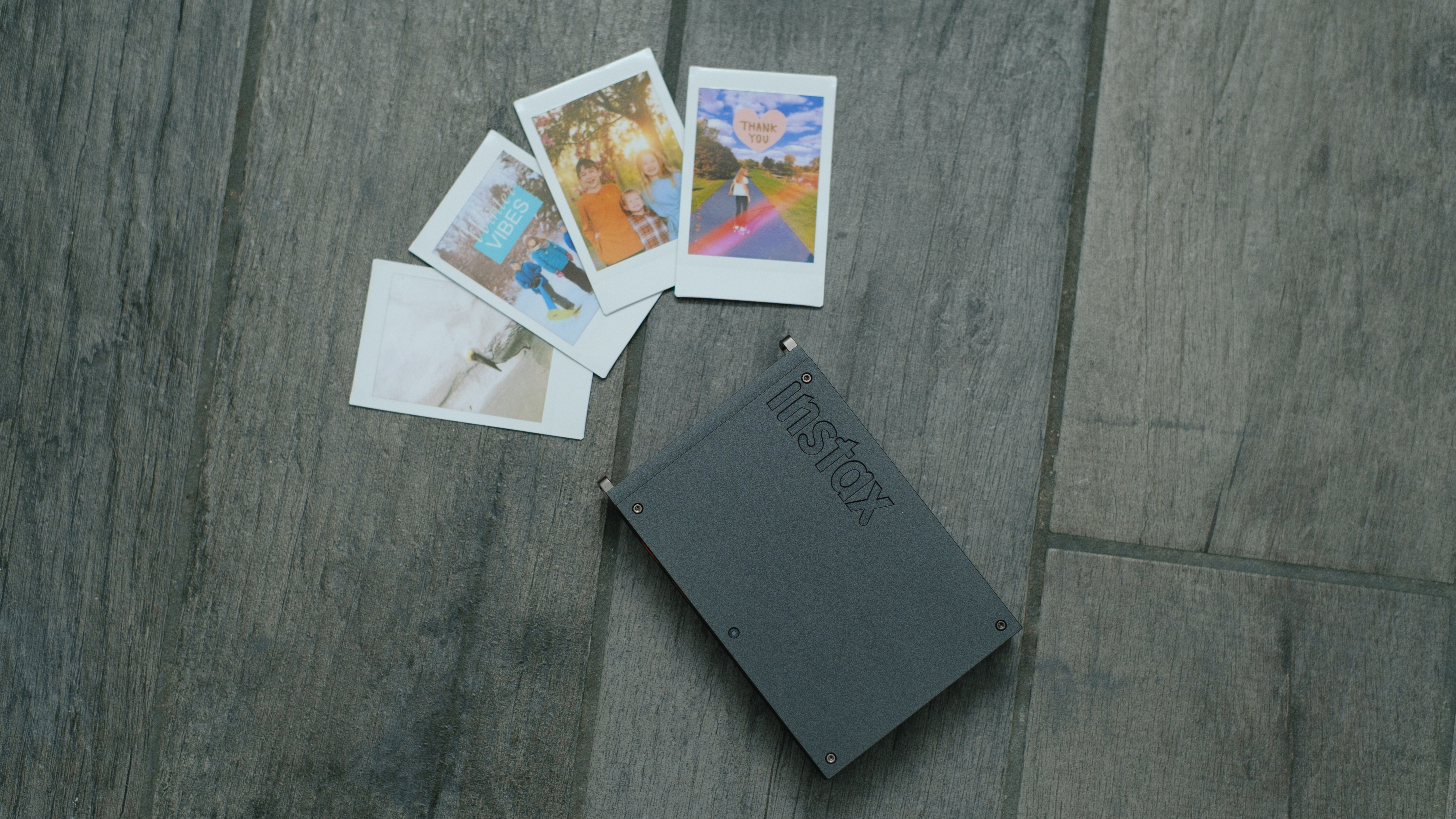 The Fujifilm Instax Mini Link+ on a gray background with instant prints
