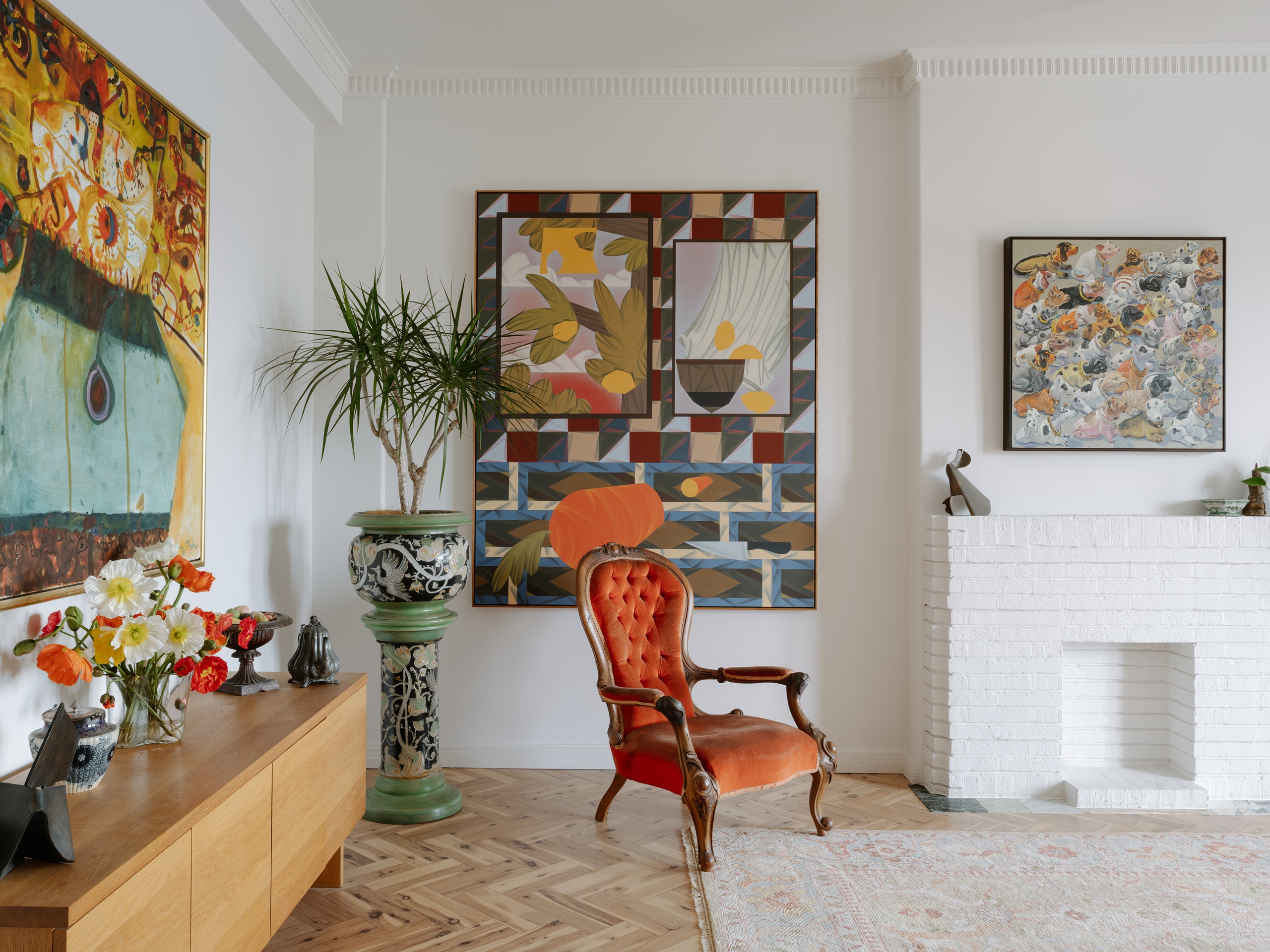 a living room with lots of art, a traditional chair, and decorative potted plant