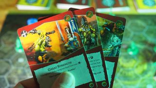 A hand holding up Warhammer Underworlds: Embergard cards in front of the board and decks