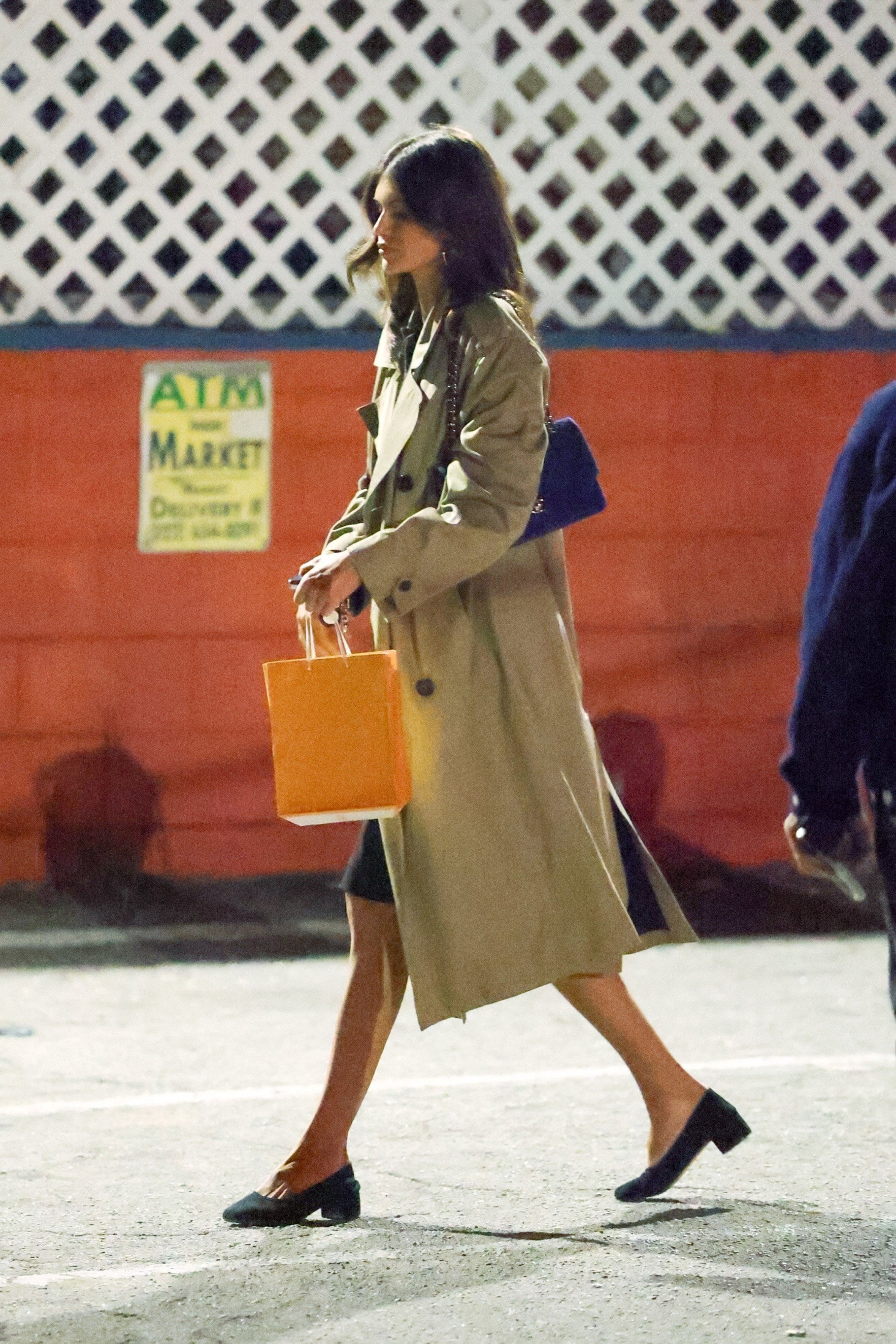 Kaia Gerber wearing a trench coat, knee length skirt, and block heels