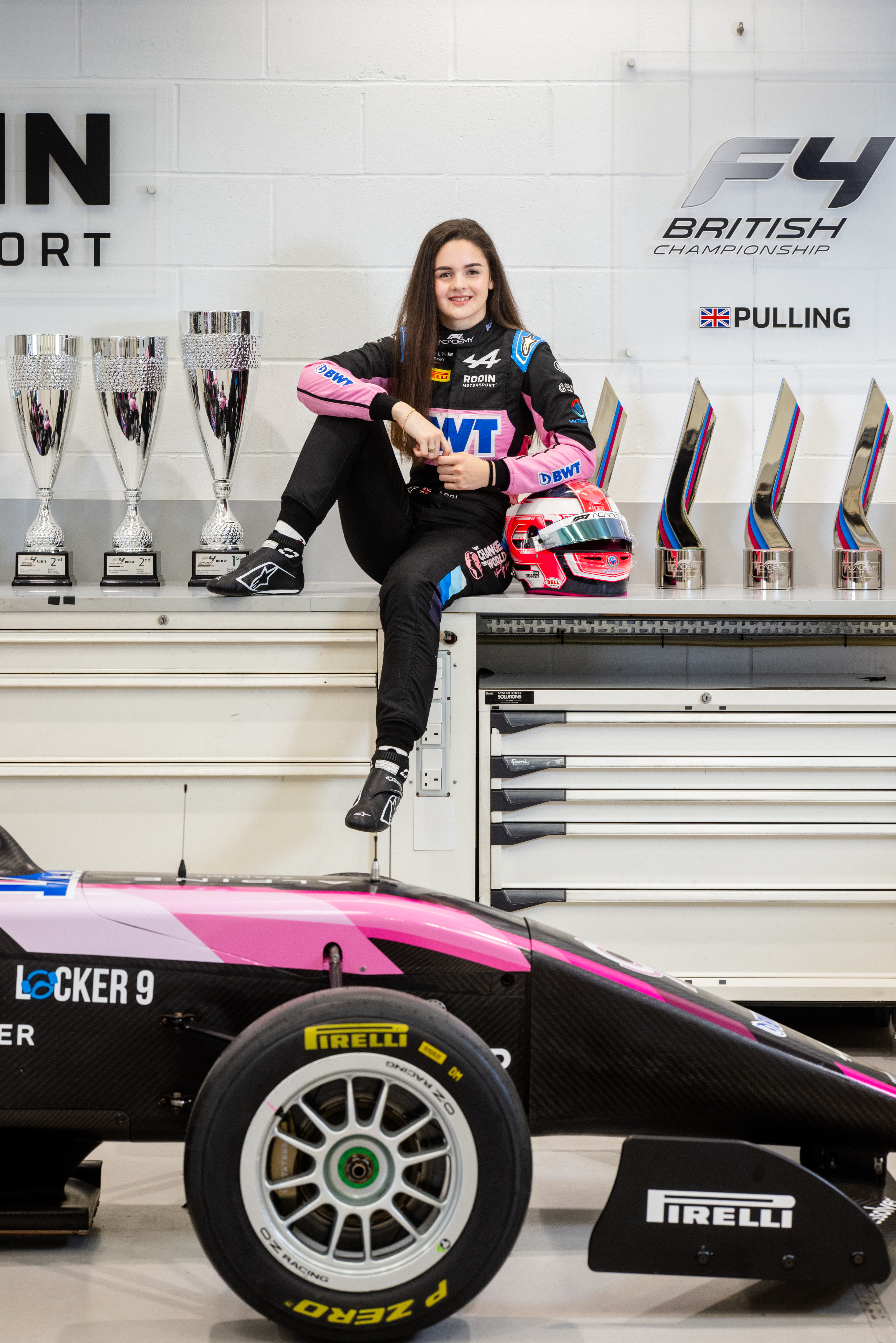 Girl in racing overalls surrounded by trophies