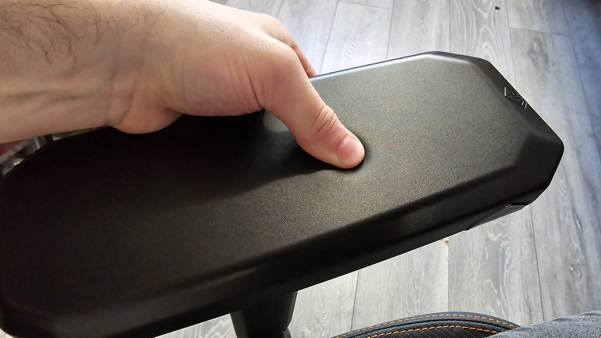 A user's thumb pressing into the armrest of an AndaSeat Kaiser 3 XL gaming chair