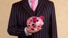 Man in a suit and tie holding a piggy bank that is full of holes