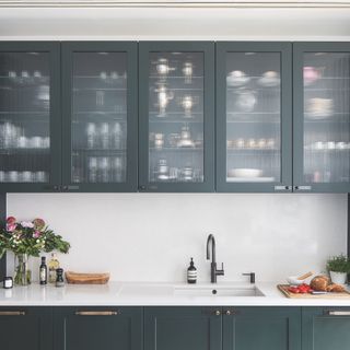 dark green kitchen with fluted glass wall cabinets