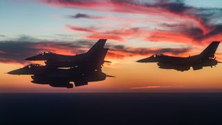 three fighter jets tightly clustered together in flight with red clouds and a sunset sky behind