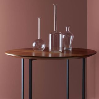 A pink-red room with a wooden side table and glass vases