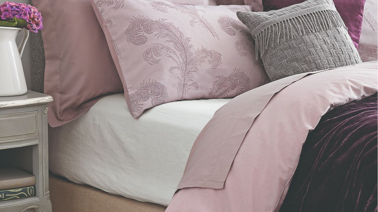 A bed with pink bedding and scatter cushions