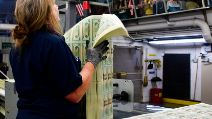 US mint worker holding sheets of $20 bills © AFP via Getty Images