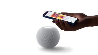 The Apple HomePod Mini in white with a hand holding an iPhone to it