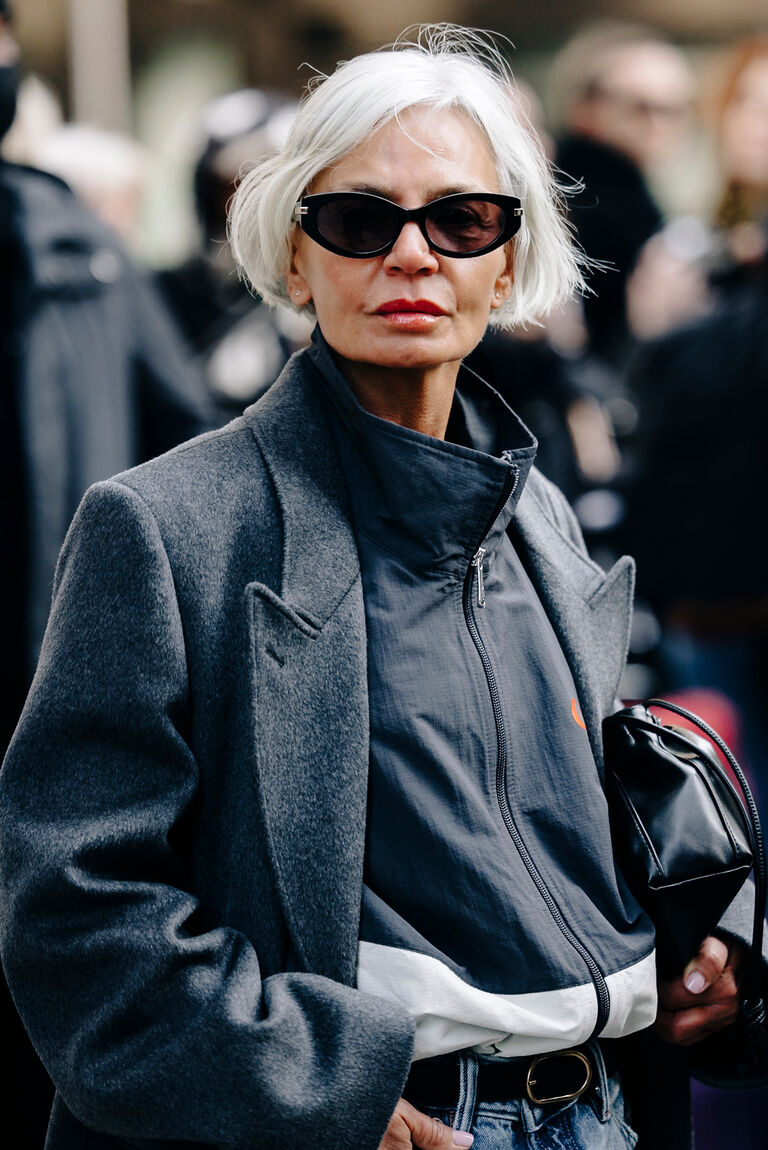 a woman at new york fashion week wearing a gray funnel-neck windbreaker jacket under a gray jacket and with blue jeans