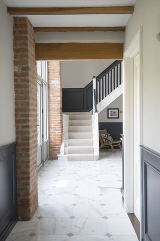 hallway/entryway with marble flooring, staircase, exposed brick and grey painted walls