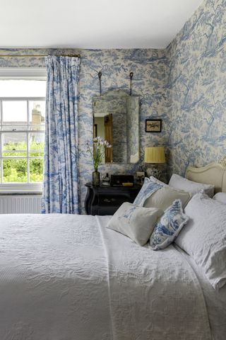 bedroom with blue toile wallpaper, curtains and lightshades