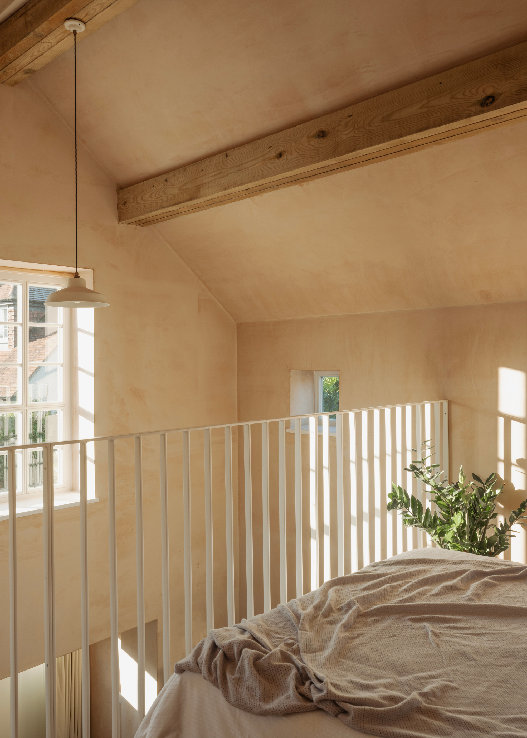 A bright sunlit open concept terrace bedroom with a pendant light, exposed beams and a potted plant