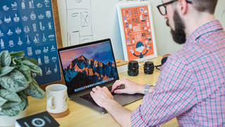 A man on a MacBook in a bright home office