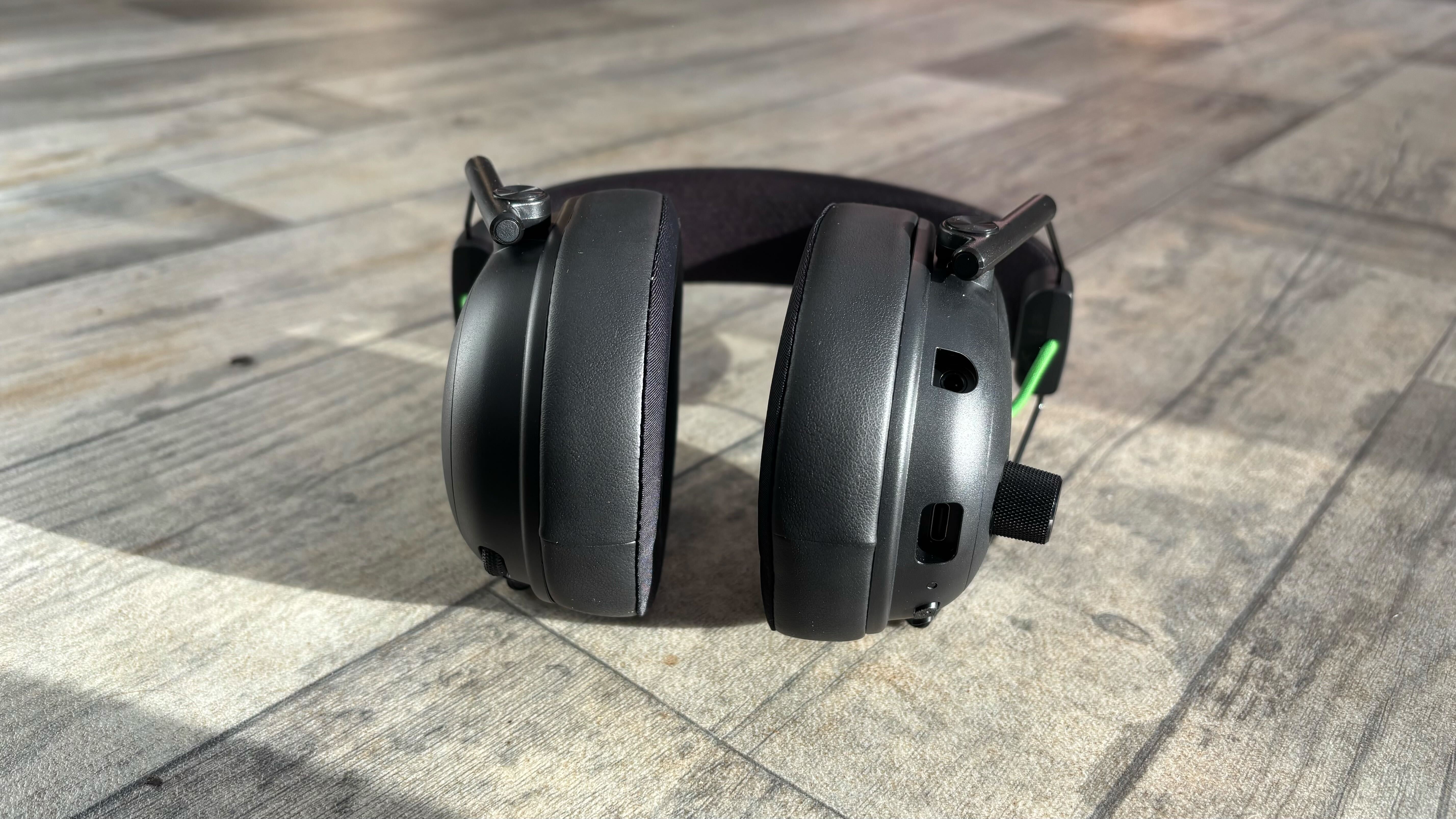 Razer BlackShark V3 wireless headset lying down on a wooden surface with the ear cups facing toward the camera