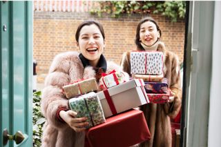 Two women stood in a doorway hold a pile of presents