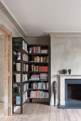 Living room with grey limewash walls, black corner bookshelf, feature fireplace and period coving