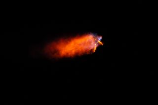 a rocket launches at night, leaving a bright plume of fire in its wake