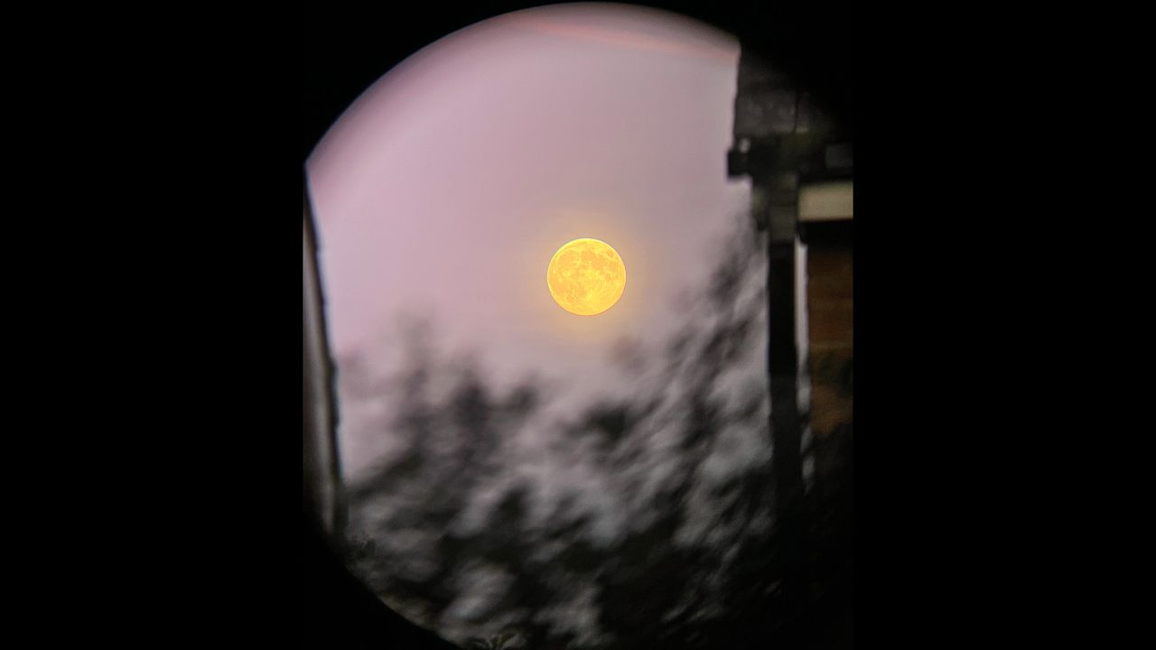 full beaver moon rising in a pink sky through binoculars