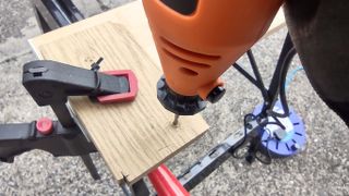 An orange rotary multi tool being used to drill a hole in wood