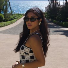 Woman wearing black Celine sunglasses, black headband, gold earrings, and white and black dress in the South of France.