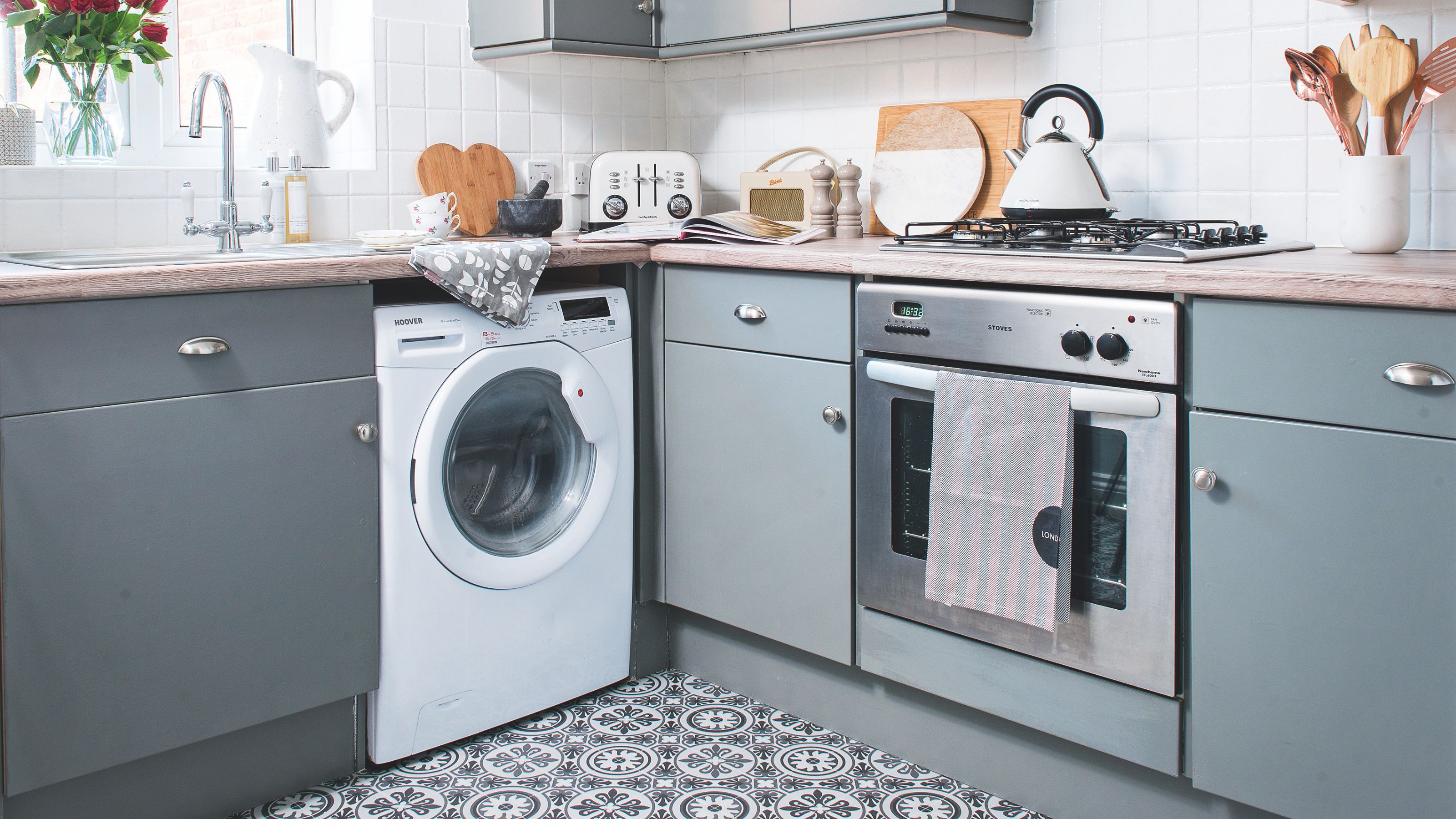 Blue kitchen with patterned tiled floor, blue cabinets and a washing machine and oven built-in