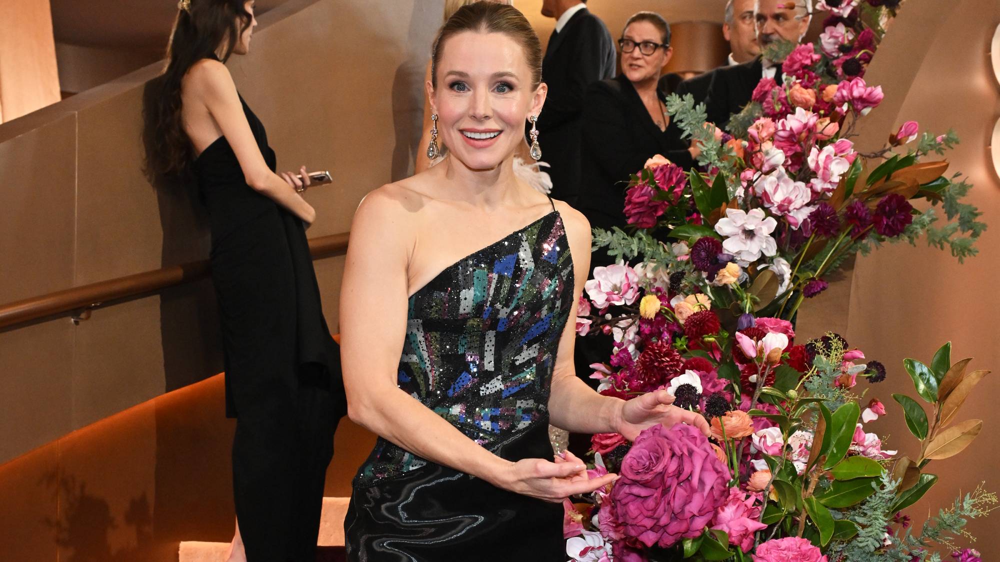 Kristen Bell pointing to a gigantic pink rose on a staircase at the Golden Globes 