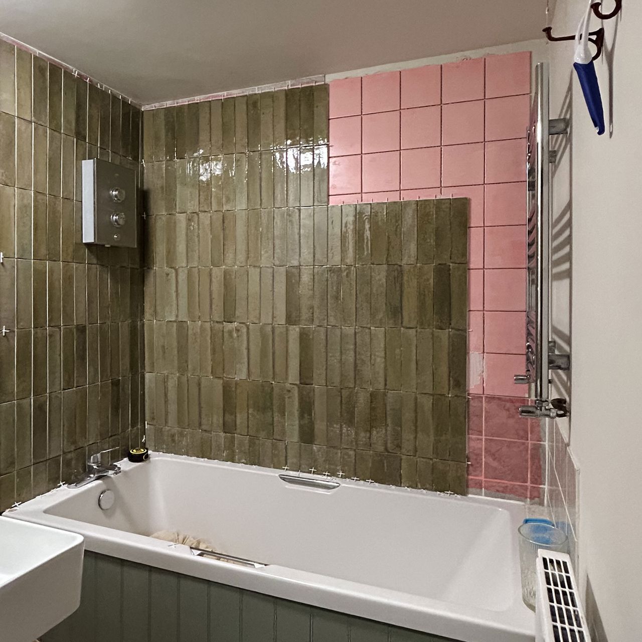 Bathroom being retiled from pink square tiles to green rectangular tiles around bath