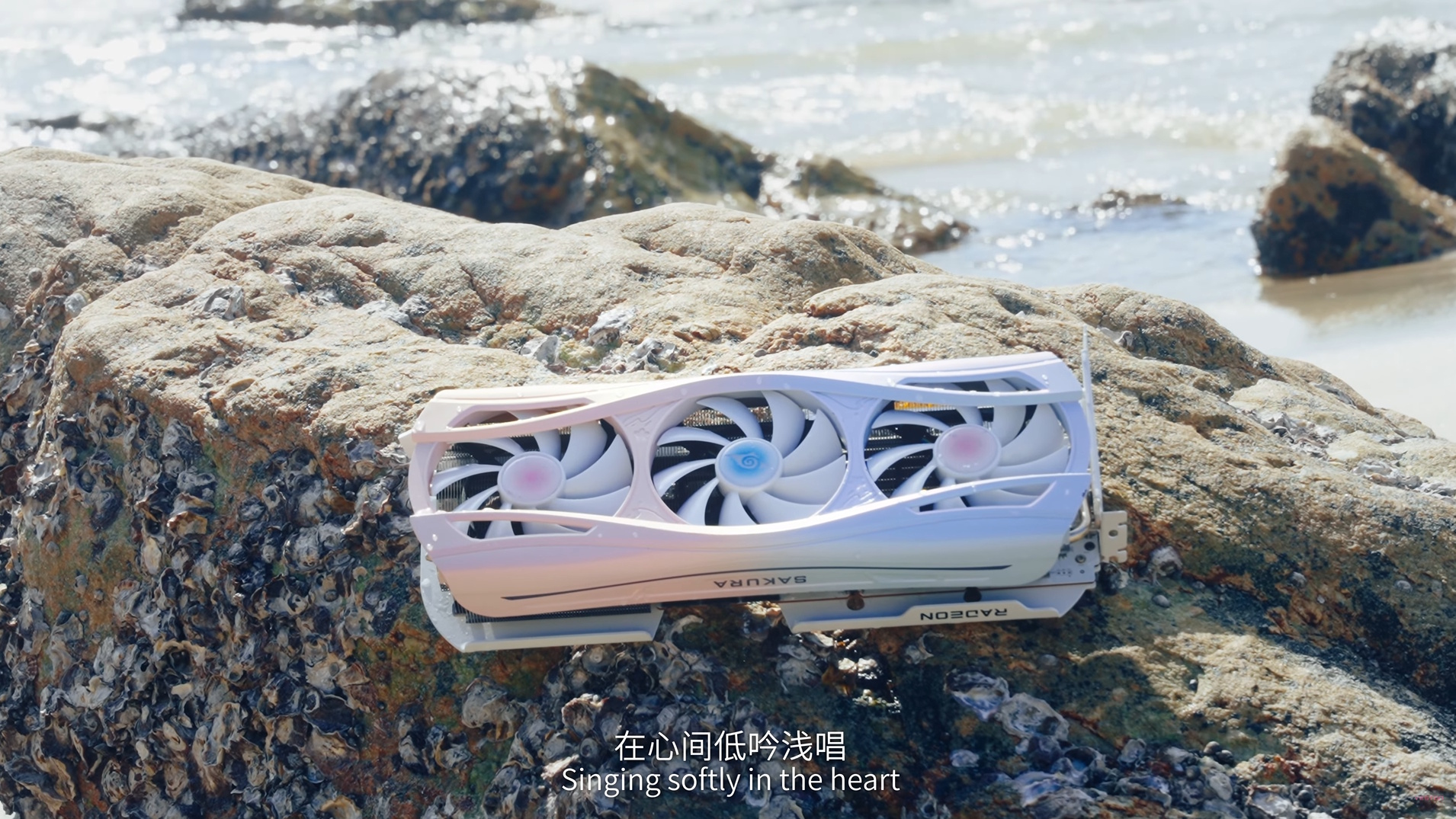 Yeston Sakura Atlantis RX 9070 XT graphics card on a rock with text saying 'singing softly in the heart'