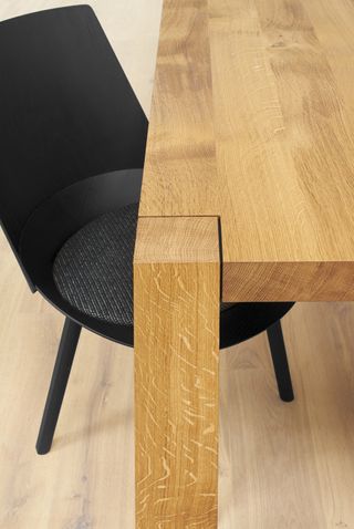 A detail of a black chair set next to a wooden table.