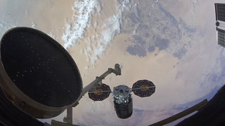 a robot arm with a spacecraft floating above earth. bits of the international space station like solar panels and modules are visible around the edges