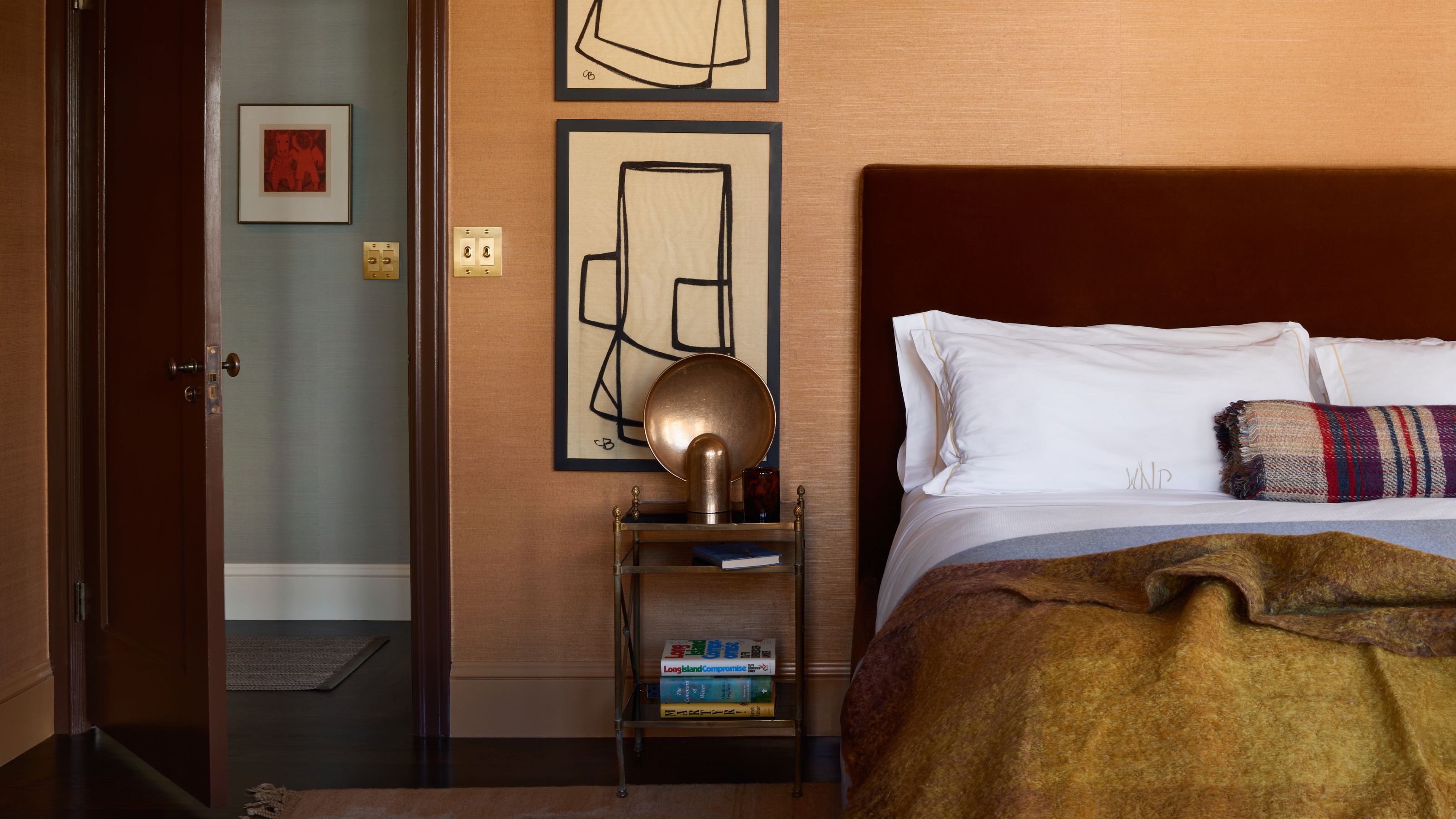 a caramel toned wallpapered bedroom with dark burgundy rust headboard and casual styling
