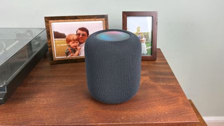 Apple HomePod (2nd Generation) on a wooden counter next to photos frames and a record player