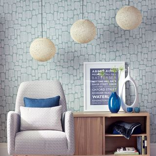 Blue retro patterned wallpaper behind armchair and wooden sideboard