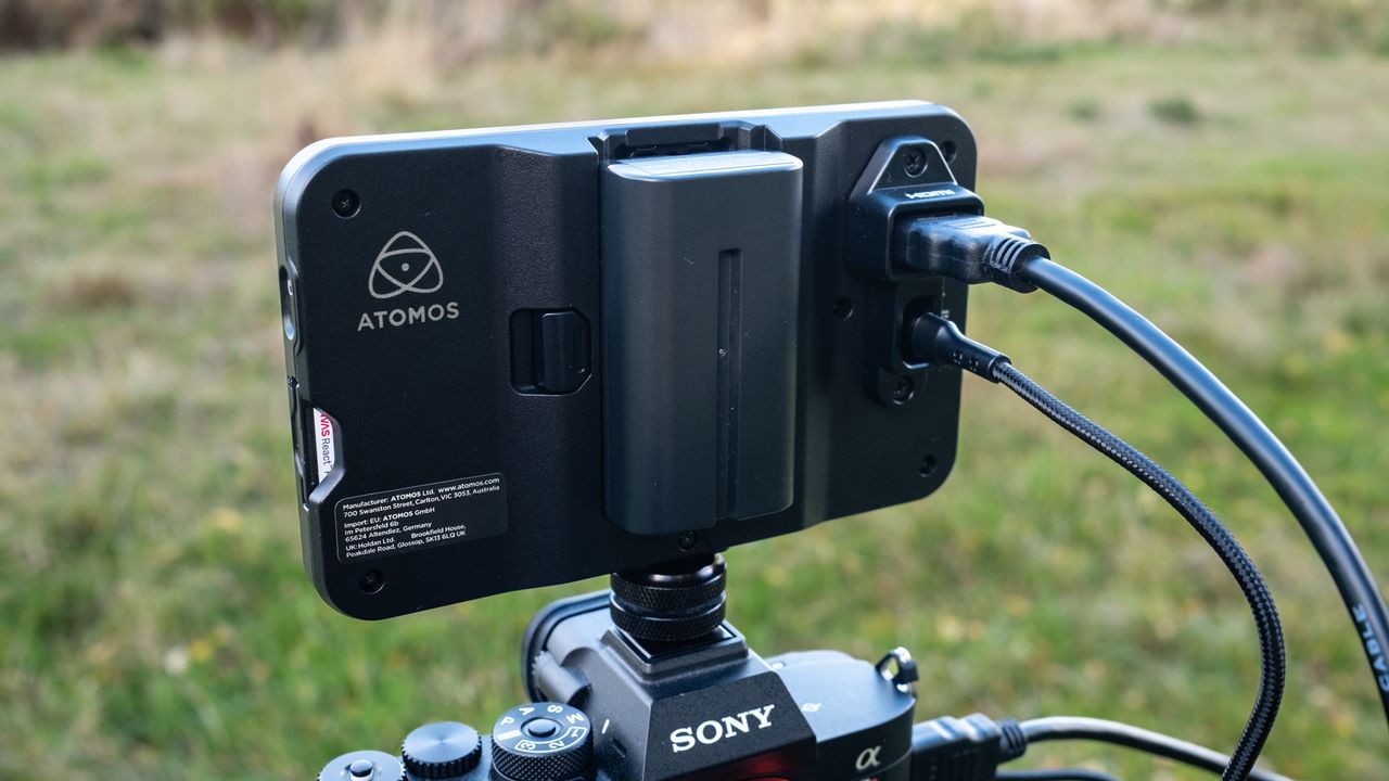 The back of an Atomos Shinobi II camera monitor showing the battery on top of a Sony camera outside in a field