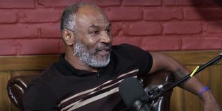 Mike Tyson wearing a black shirt and talking into a microphone while recording his podcast.