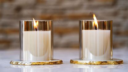 two identical, lit candles, side by side, on a surface