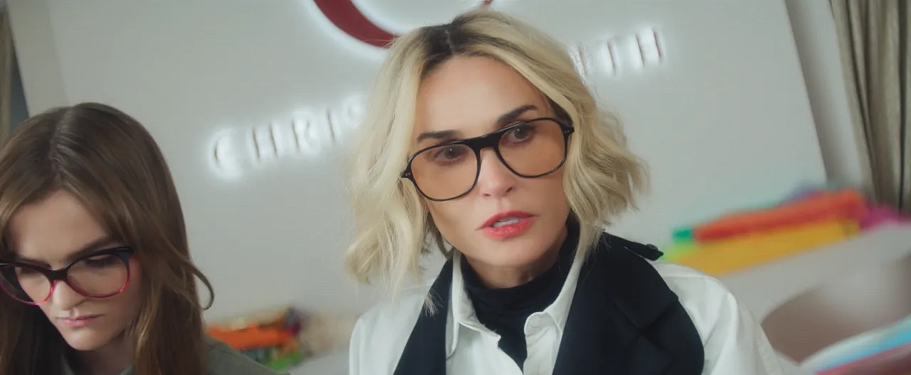 A woman in a blonde bob (Demi Moore as Christie Smith) stands with a brunette woman in front of a wall with a &amp;quot;Christie Smith&amp;quot; logo. Everything in the image is tilted diagonally, in 'I Love Boosters.'