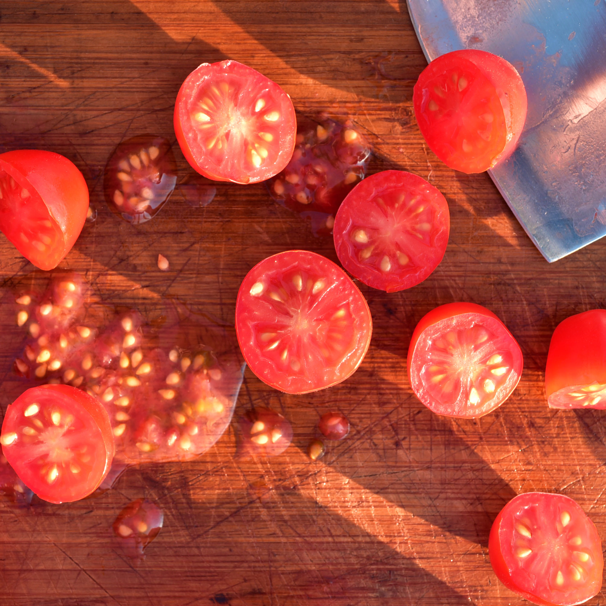 sliced tomatoes and seeds on chopping board with large silver blade