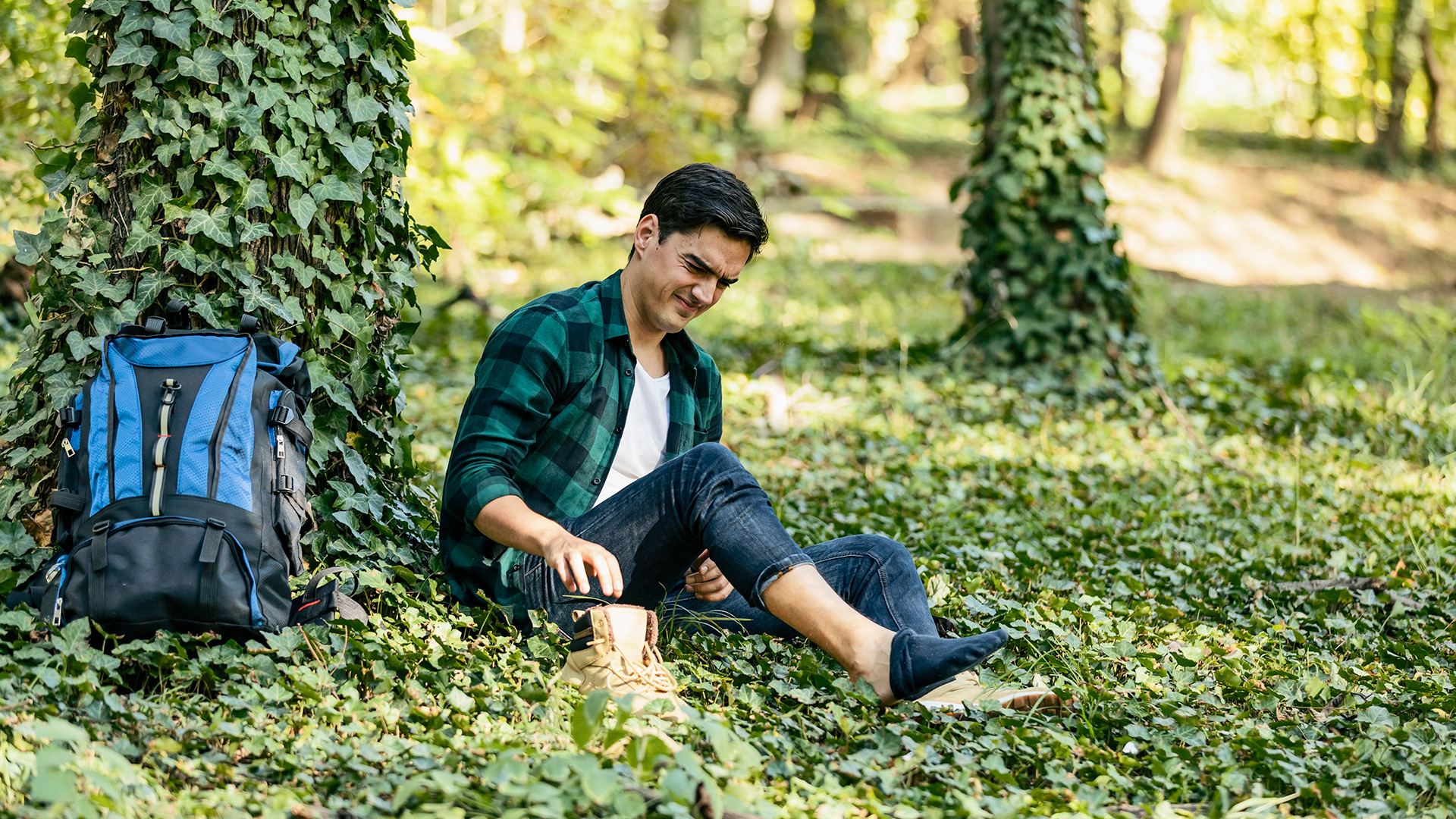 Man sat down by a tree with his boot off, looking uncomfortable