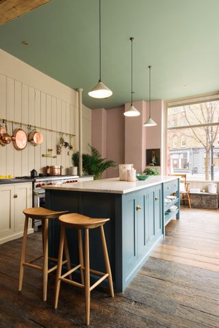 Three pendant lights over a blue island in a green and pink kitchen design.